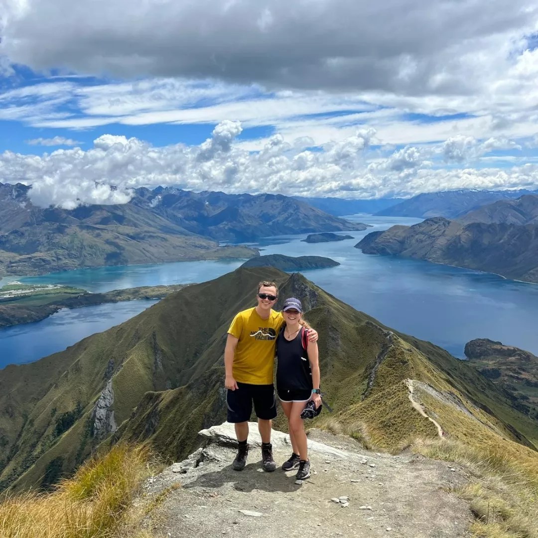 Woman standing on a mountain overlooking a lake, representing wellbeing, clarity and a balanced lifestyle