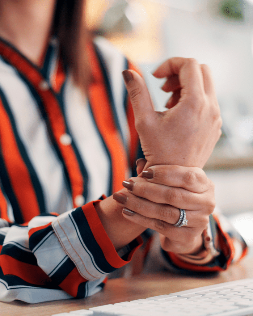 A close-up of a person rubbing their wrist with one hand while wearing a striped shirt, showcasing a ring on one hand.
