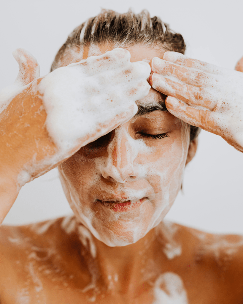 Person applying foam cleanser to their face with eyes closed, surrounded by bubbles.