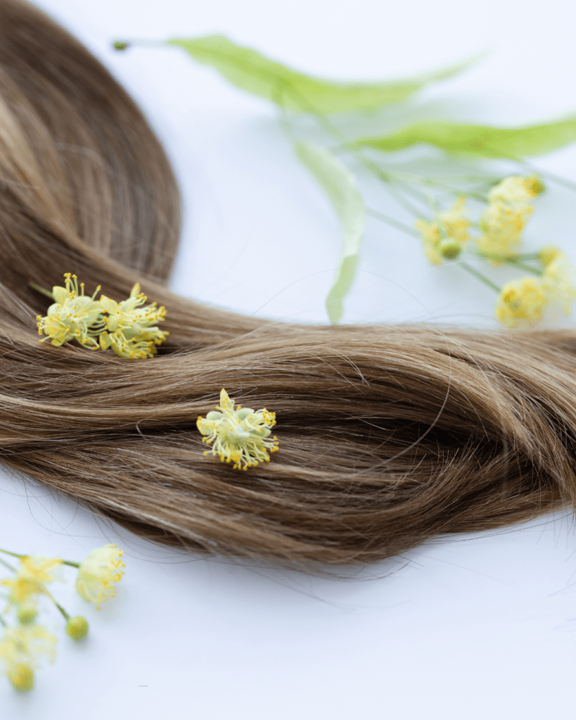 A close-up of long, brown hair adorned with delicate yellow flowers and green leaves on a white background.