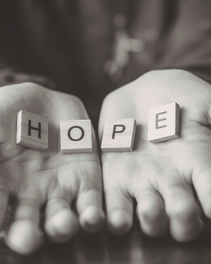 Hands holding wooden blocks that spell the word 'HOPE'.