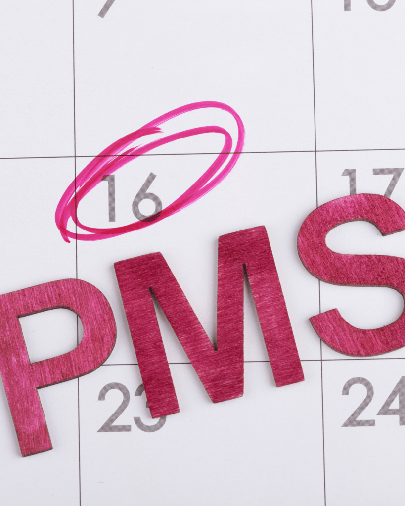 Close-up of a calendar page with the date 16 circled in pink and the letters 'PMS' in pink wood.
