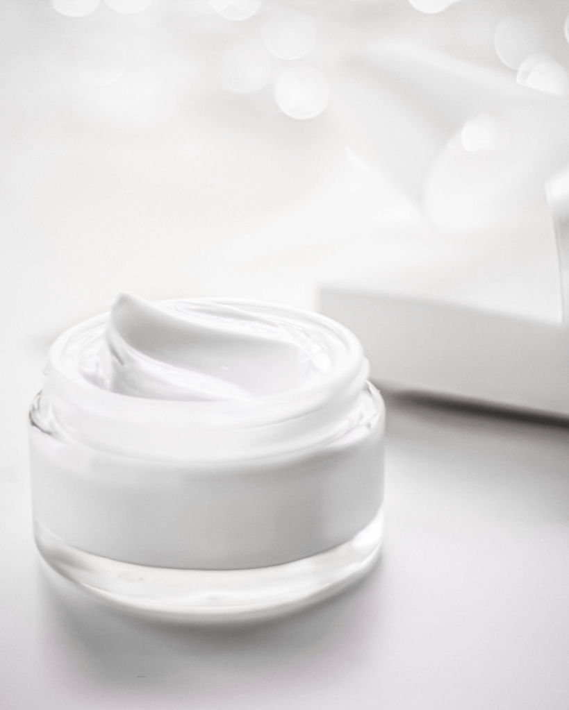 A small glass jar of moisturizing cream with a smooth white texture, placed on a light background.