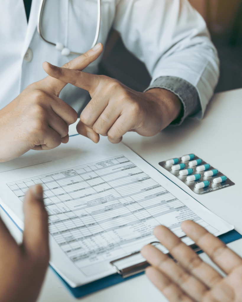 A healthcare professional discussing a patient chart and medication options, with a clear focus on a prescription pad and a blister pack of pills.