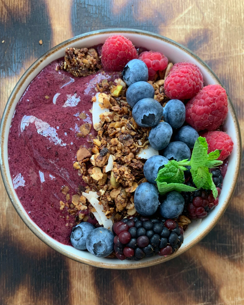 A delicious acai bowl topped with granola, blueberries, blackberries, raspberries, and a sprig of mint.