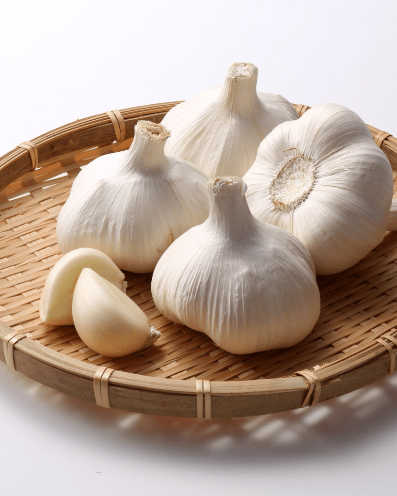 A woven bamboo basket containing several heads of garlic, including whole bulbs and individual cloves.