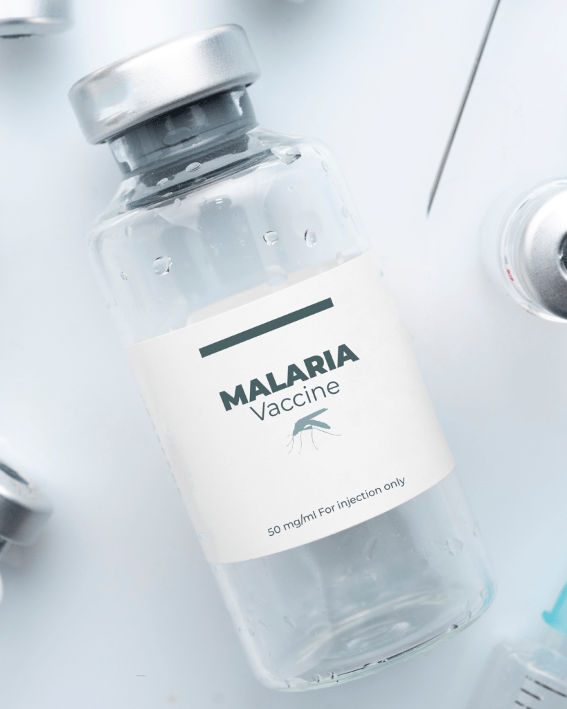 A clear glass vial labeled 'MALARIA Vaccine' with a dosage of '50 mg/ml For injection only.' The vial is surrounded by other medical items.