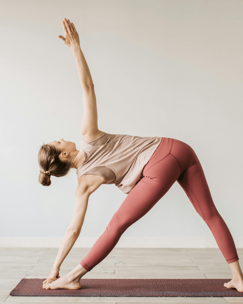 A woman performing a yoga pose, reaching one arm towards the ceiling while bending sideways on a yoga mat, dressed in a tank top and leggings.