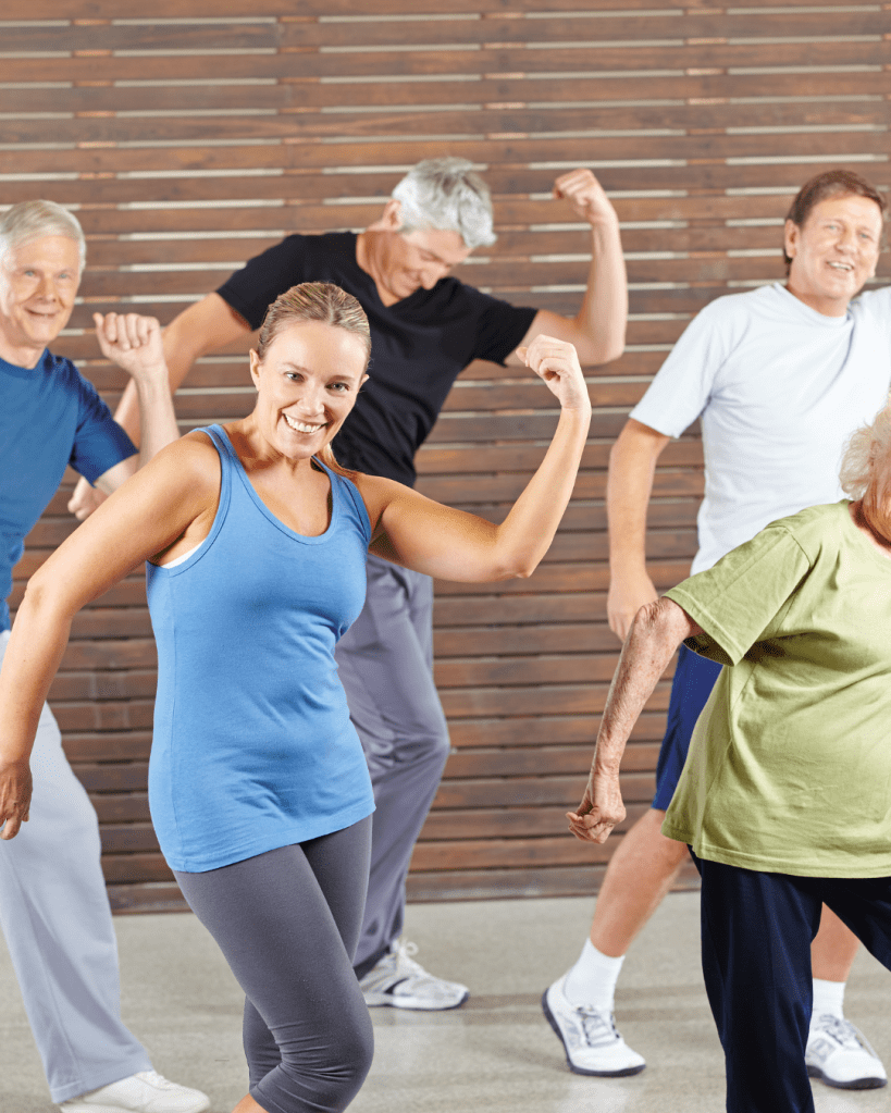 A group of older adults engaging in a fun exercise session, smiling and flexing their muscles, with a wooden backdrop.