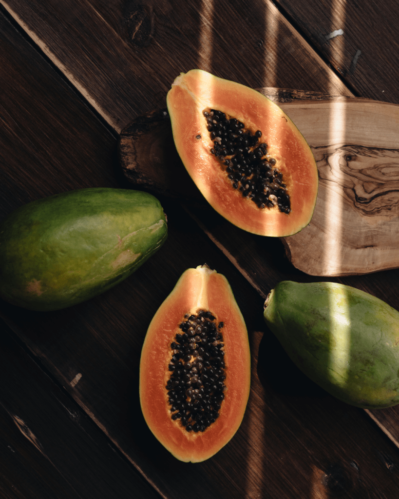 Fresh papaya fruit, including whole and sliced pieces, showcasing vibrant orange flesh and black seeds, arranged on a wooden surface.
