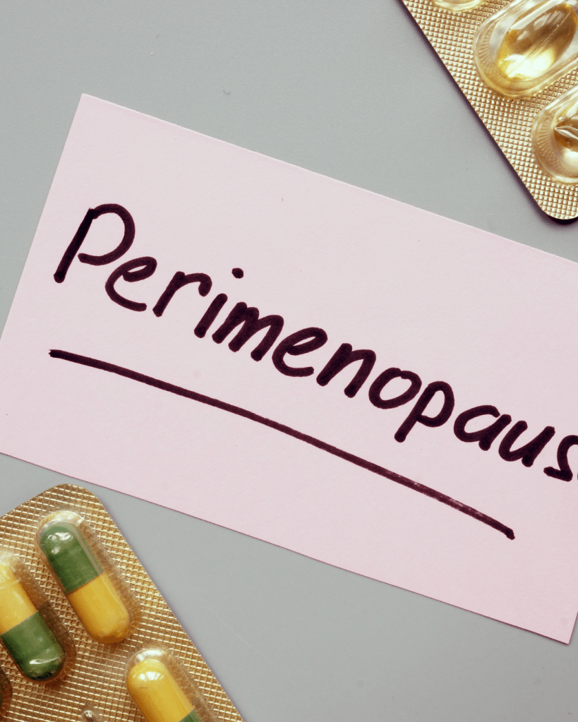 A pink note card with the word 'Perimenopause' written in black, placed near a strip of yellow and green capsules.