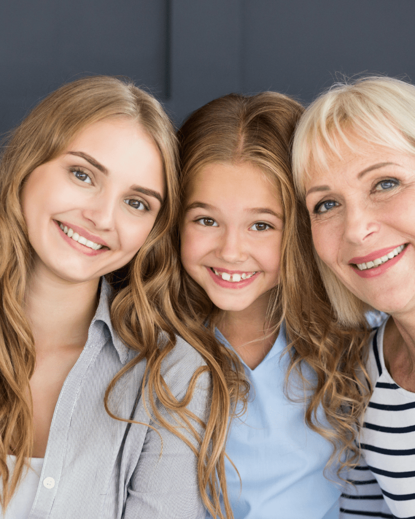 A smiling young woman, a girl, and an older woman posing close together, showcasing their happy expressions in a friendly setting.