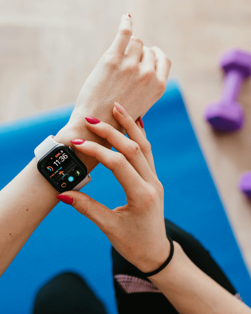 Person checking a fitness smartwatch on their wrist while sitting on an exercise mat.