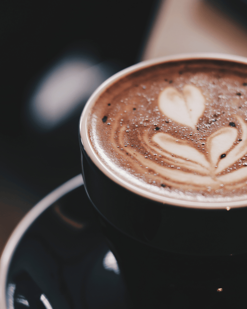 Close-up of a coffee cup featuring latte art with heart shapes on the surface.
