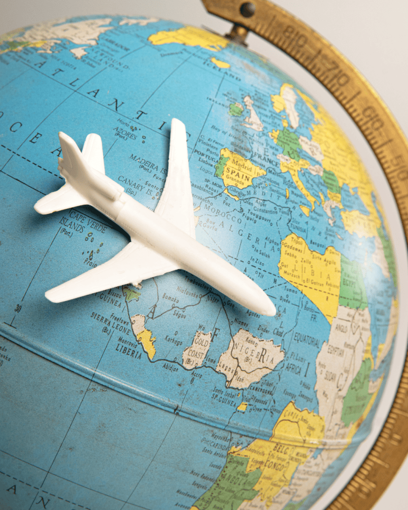 A white model airplane positioned on a colorful globe, illustrating various countries and continents.
